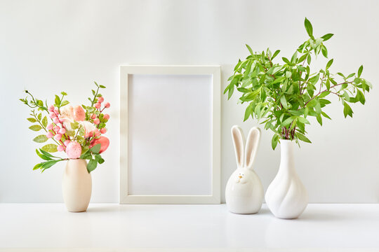 Home interior with easter decor. Mockup with a white frame and branches with green leaves in a vase on a light background