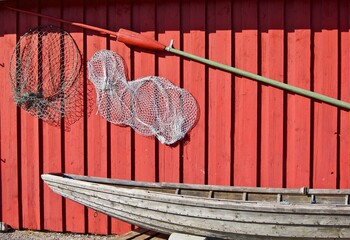 Fishing equipment hanging on a red building wall behind an old wooden boat.