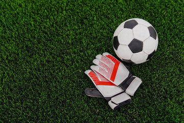 Soccer ball and goalkeeper gloves on football field. Copy space.