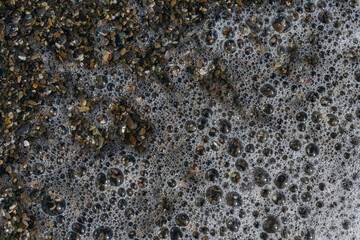 top view of a foamy sea wave breaking on a summer pebble beach
