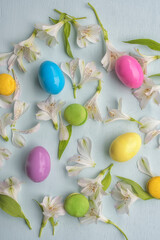 Fototapeta na wymiar Delicate Easter background of white flowers, petals of colored macaroons and colored eggs. Spring gentle background.