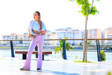 Portrait of beautiful blonde teenager girl with cool pigtails , white t-shirt and flared pink pants skating on rollers in park