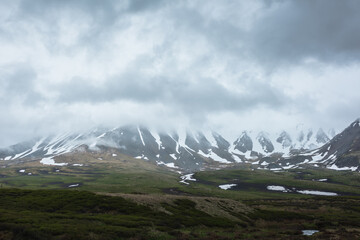 Dramatic alpine landscape with snowy mountains in gray low clouds. Bleak atmospheric scenery of...