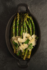 Fried green asparagus with parmesan in a pan.  Top view. Dark background.