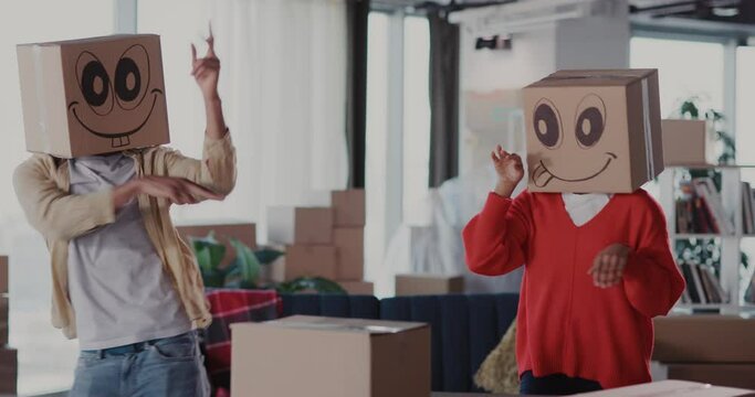 Casual carefree happy dating couple of man with woman wearing carton boxes on heads with faces having fun celebrating hoiday in new home.