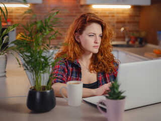 Beautiful young woman in casual clothes using laptop and smiling while working indoors, sitting next to hot coffee. technology woman concept for alternative freelance office