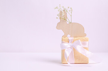 Easter symbol wooden hare with a branch of hepsophila on a gift box on a white background.