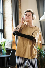 Girl with prosthetic arm enjoying music in wireless headphones and dancing during leisure time at home