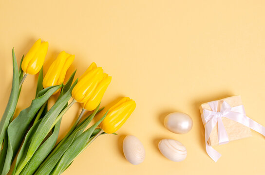 A bouquet of tulips, Easter eggs and a gift box on a yellow background