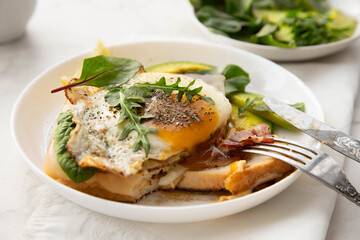 Croque madame sandwich with cheese, avocado and arugula close-up on a white plate.