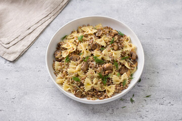 Traditional Jewish dish kasha varnishkes: buckwheat, pasta, champignon mushrooms, fried onions with herbs on a gray textured background, top view