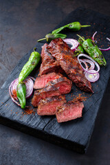 Traditional barbecue sirloin steak with chili and onion rings served as close-up on a charred wooden board