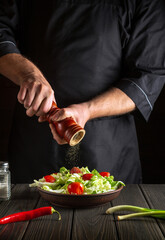 Professional chef adds peppers to a fresh vegetable salad in a kitchen. Close-up of cook hands holding a mill. The concept of cooking delicious food