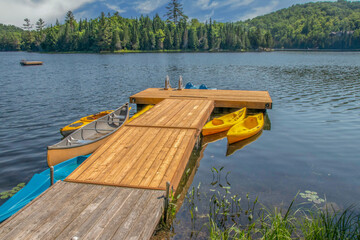 Long wooden dock at a cottage on lake, canoes and kayaks, forested island in background, nobody