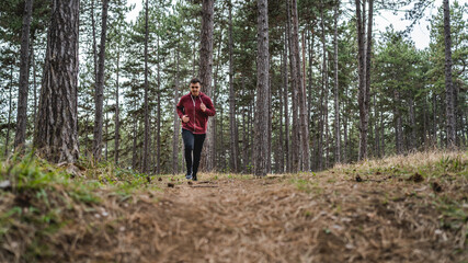 Naklejka na ściany i meble Front view full length of one man young caucasian male running trough the woods in nature outdoor jogging in autumn or spring day - sport fitness and recreation concept real people copy space