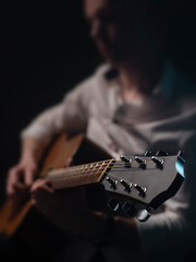 The guitarist is playing acoustic guitar shown in small depth of field where the focus is on the headstock. Dark and moody.