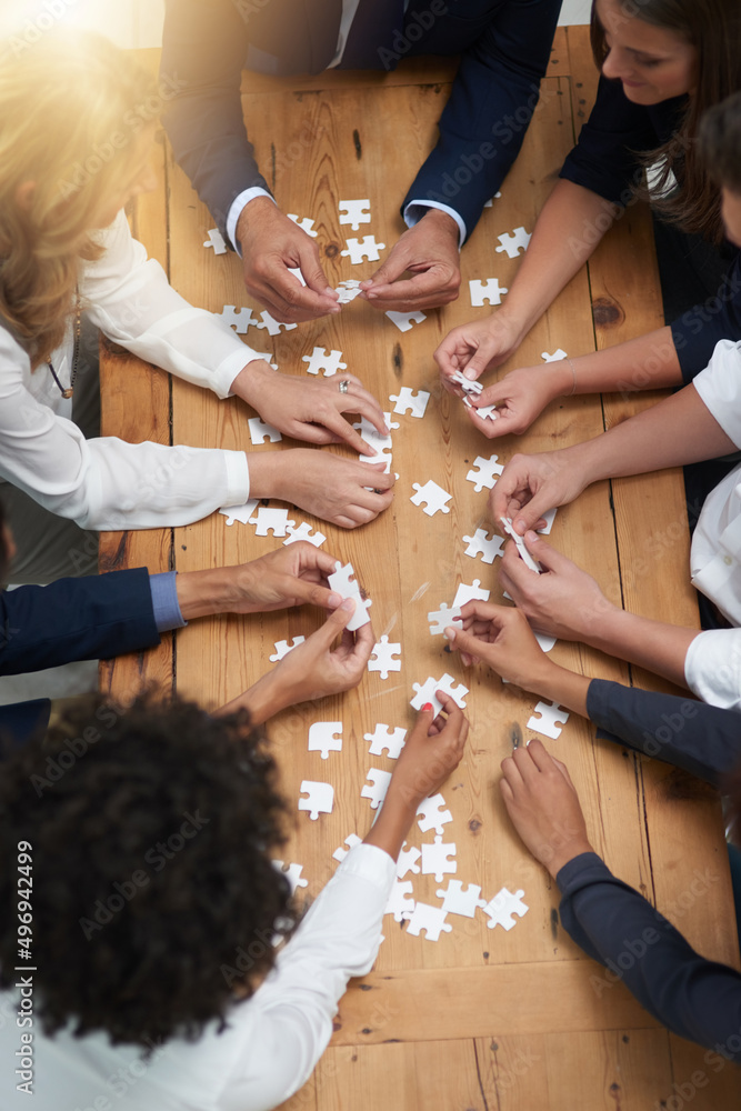 Poster finding solutions piece by piece. high angle shot of a group of businesspeople building a puzzle tog