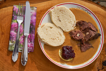 Roasted fallow deer venison in sour cream sauce served with traditional czech bread dumplings, slice of lemon and cranberry marmelade. Old and traditional seasonal dish from cuisine of Czech Republic.