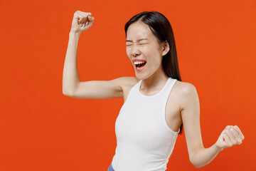 Young woman of Asian ethnicity 20s years old in white tank top doing winner gesture celebrate...