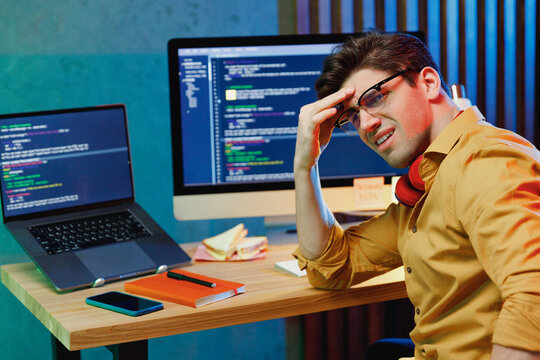 Side view young confused sad software engineer IT specialist programmer man in shirt work at home writing code on laptop pc desktop computer checking virus look camera. Program development concept