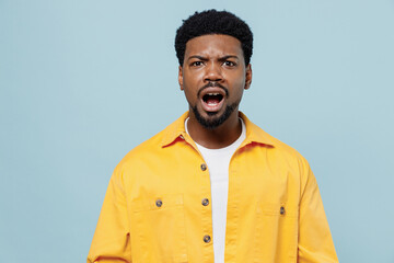 Young confused shocked sad man of African American ethnicity 20s wear yellow shirt look camera with open mouth isolated on plain pastel light blue background studio portrait. People lifestyle concept.