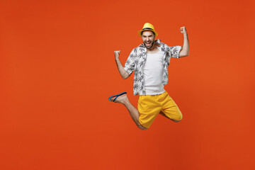 Obraz premium Full body overjoyed happy young tourist man wear beach shirt hat jump high do winner gesture clench fist isolated on plain orange background studio portrait. Summer vacation sea rest sun tan concept.