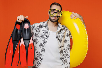 Young smiling tourist man wear beach shirt goggles hold inflatable ring flippers travel abroad on weekends isolated on plain orange background studio portrait Summer vacation sea rest sun tan concept