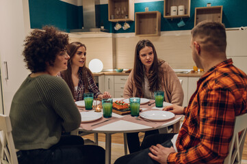 Group of friends enjoying dinner while sitting at the kitchen table together
