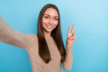 Self-portrait of attractive cute cheerful girl good mood showing v-sign isolated over bright blue...