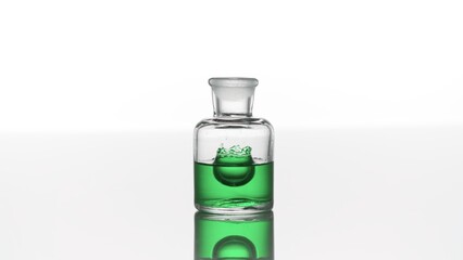 Drop of eucalyptus oil falls down into clear old fashioned bottle with green transparent liquid making crown inside a bottle | Abstract cosmetics with eucalyptus oil formulation concept