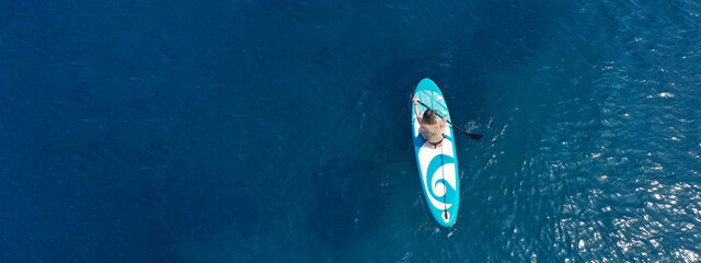 Aerial drone ultra wide panoramic photo with copy space of fit unidentified woman paddling on a SUP...