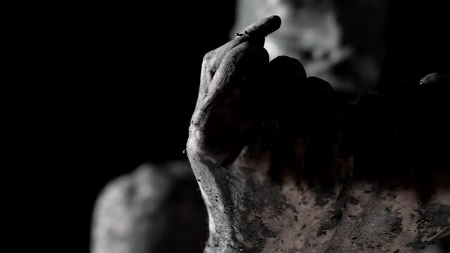 woman with bandaged eyes is covered by grey dirt or clay, closeup view of hands, face and body