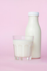 A bottle and a glass of white milk, highlighted on a pink background, close-up.