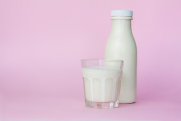 A bottle and a glass of white milk, highlighted on a pink background, close-up.