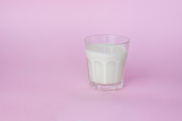 A glass of white milk, highlighted on a pink background, close-up.