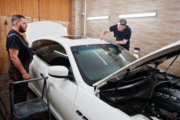 Worker in detailing garage put polyurethane anti-gravel film cover in white luxury car.