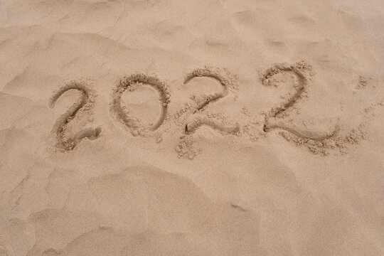 Inscription 2022 on sea or ocean shore. Drawing on sand surface texture. Top view, copy space.