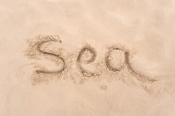 Inscription ''Sea'' on sea or ocean shore. Drawing on sand surface texture. Top view, copy space. Vacation and relax concept