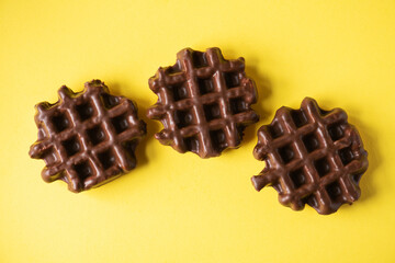 Three chocolate waffles on a yellow background, flat lay, top view.