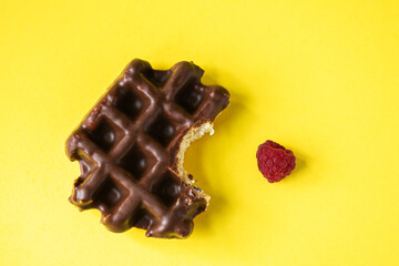 Bitten off chocolate waffle and raspberry, yellow background, top view. - 496952097
