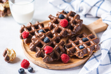 Chocolate waffles and berries on a wooden plate on a wooden baclground.
