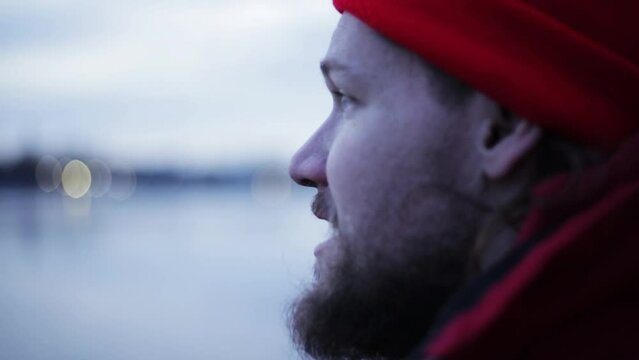 serious bearded caucasian man captain of a fishing ship in a red hat and jacket amid port lights and water gives orders to his team.
