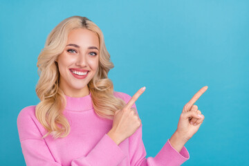 Photo of cute young wavy blond lady indicate empty space wear pink pullover isolated on blue color background