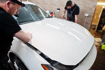 Worker in detailing garage put polyurethane anti-gravel film cover in white luxury car.