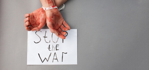 Bound bloody male hands on a gray background next to the inscription Stop the war. The topic of...