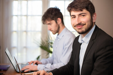 jeunes employés ou hommes d'affaires qui travaillent côte à côte au bureau avec des ordinateurs portables. Ils collaborent et travaillent en équipe. Sourire et réussite de la carrière.