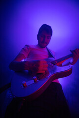 Obraz premium jeune homme qui joue de la guitare électrique en concert, dans une ambiance rock avec des lumières et de la fumée. Il prend du plaisir à jouer du rock et du blues.