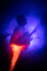 Obraz na płótnie Canvas jeune homme qui joue de la guitare électrique en concert, dans une ambiance rock avec des lumières et de la fumée. Il prend du plaisir à jouer du rock et du blues.
