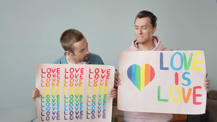 Two young handsome guys let up lgbt posters, look at each other and smile