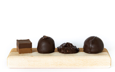 Four chocolate candies of different shapes and flavors placed on wooden plank on white background.